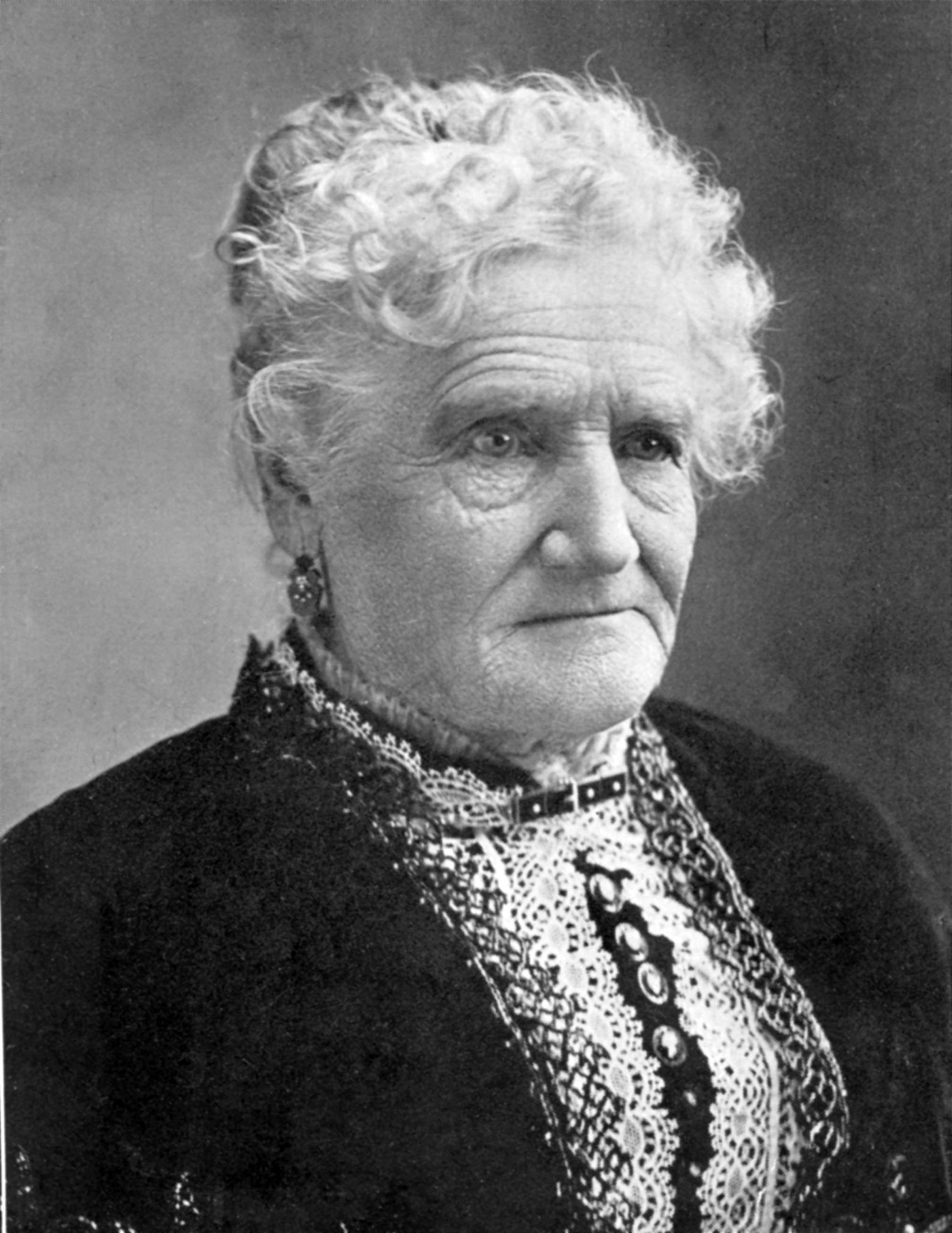 woman seated, facing the camera, in a dark shirt with lace collar